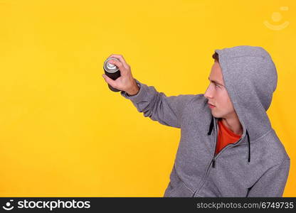 teenager wearing hoodie against yellow background holding spray