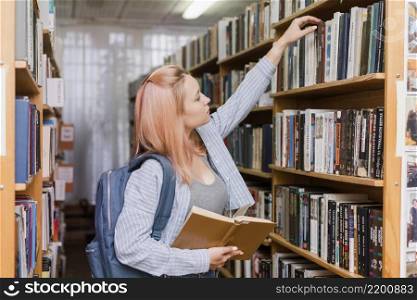 teenager with backpack picking book from bookcase