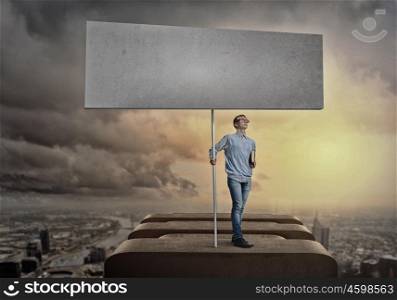 Teenager with banner. Young man against city background holding blank banner. Place for text