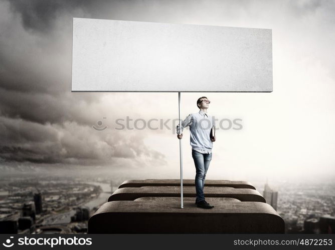 Teenager with banner. Young man against city background holding blank banner. Place for text