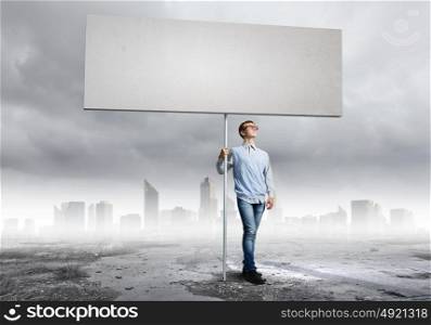 Teenager with banner. Young man against city background holding blank banner. Place for text