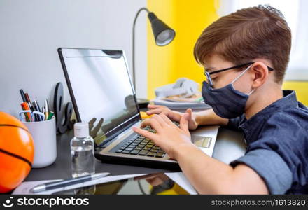 Teenager with face mask doing homework with laptop in his bedroom