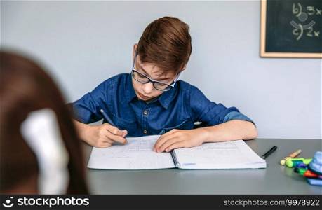 Teenager writing in his notebook at school. Selective focus on boy in background. Teenager writing in notebook at school