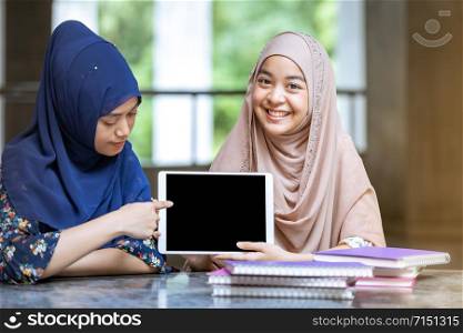 Teenager Young Adult Asian Thai Muslim university college students holding digital tablet and pile of books using for education and online education concept