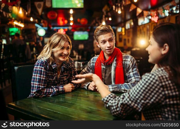 Teenagers sitting at the table in sports bar. Football fans, game tv broadcasting, young friends leisures in pub