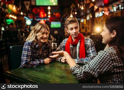 Teenagers sitting at the table in sports bar. Football fans, game tv broadcasting, young friends leisures in pub