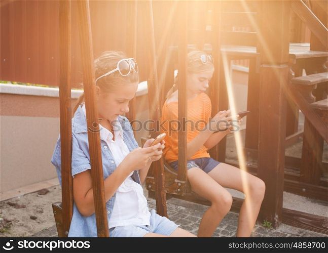 Teenagers with gadgets sitting on the swings. Teenagers with gadgets