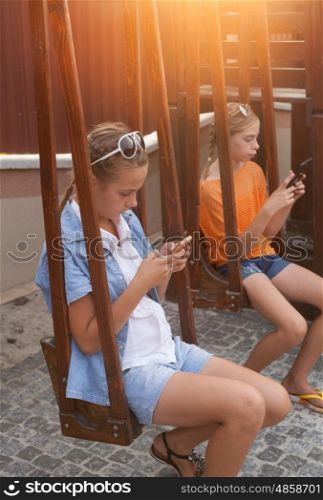 Teenagers with gadgets sitting on the swings. Teenagers with gadgets