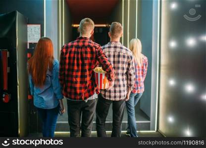 Teenagers with popcorn stands in cinema hall before the screening, back view. Male and female youth in movie theater