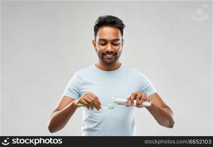 teeth cleaning, dental care and hygiene concept - smiling young indian man with toothbrush and toothpaste over grey background. indian man with toothbrush and toothpaste