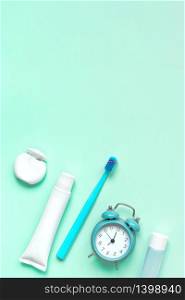 Teeth hygiene and oral care products and alarm clock on green neo mint color background with copy space. Blank tube of toothpaste, dental floss and toothbrush. Flat lay, top view composition, mockup