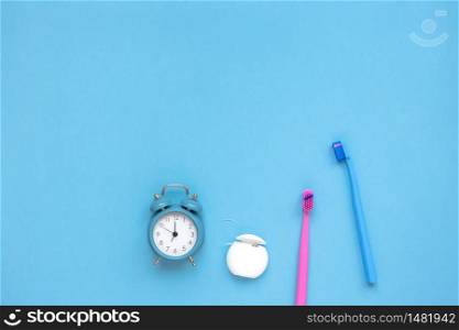 Teeth hygiene and oral dental care products and alarm clock on blue color background with copy space. Two family toothbrushes. Flat lay, top view composition, mockup. Morning routine concept