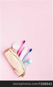 Teeth hygiene and oral dental care products in golden travel cosmetic purse kit on pastel pink color background with copy space. Blank tube of toothpaste and toothbrushes. Flat lay, top view composition