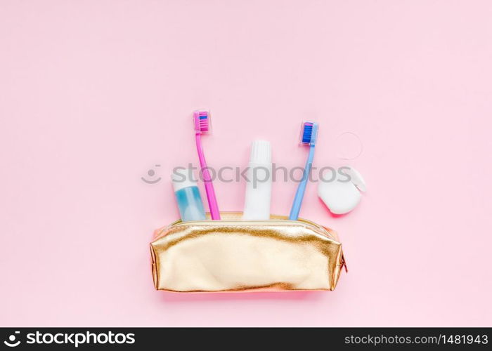 Teeth hygiene and oral dental care products in golden travel cosmetic purse kit pastel pink color background with copy space. Blank tube of toothpaste and toothbrushes. Flat lay, top view composition