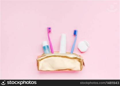 Teeth hygiene and oral dental care products in golden travel cosmetic purse kit pastel pink color background with copy space. Blank tube of toothpaste and toothbrushes. Flat lay, top view composition