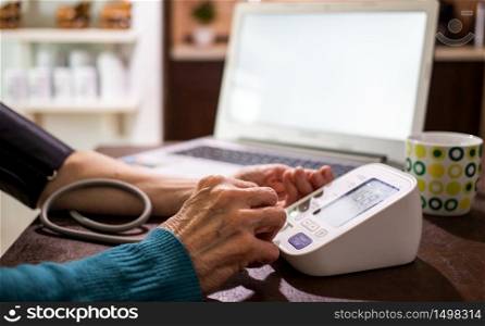 telemedicine concept elderly woman in an online consultation on video call from her kitchen taking her blood pressure