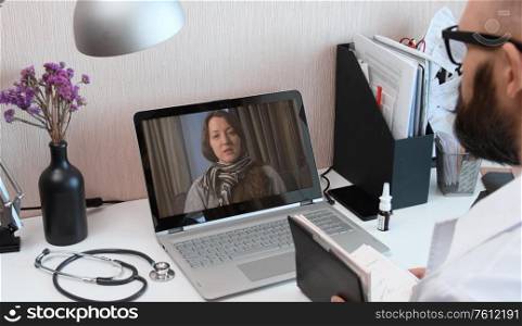 Telemedicine. Consultation with physician through mobile video call. Doctor talking to comlaining patient using video chat application on laptop and writes down symptoms.. Telemedicine. Video call with doctor