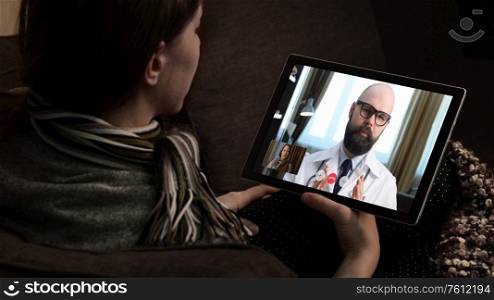 Telemedicine. Consultation with physician through mobile video call. Woman sitting on couch at home and talking to MD on tablet screen.. Telemedicine. Video call with doctor