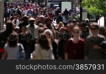 Telephoto shot with a backlit crowd of people on a wide sidewalk, walking in slow motion