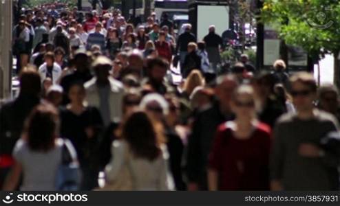 Telephoto shot with a backlit crowd of people on a wide sidewalk, walking in slow motion