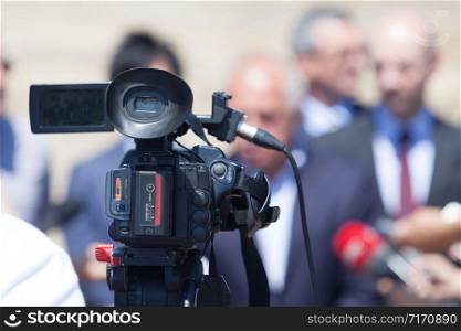 Television camera at press conference, blurred politicians or business persons in the background