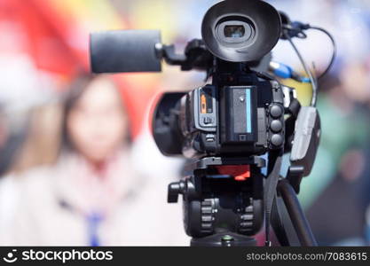 Television camera in the focus, blurred female journalist in the background. TV broadcasting.