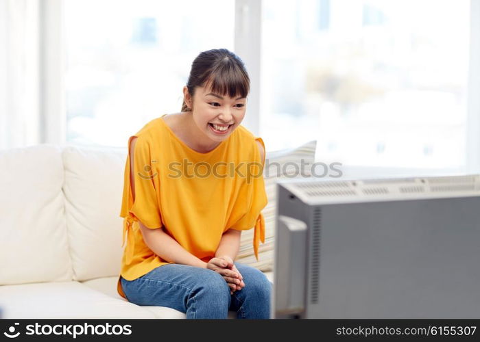 television, entertainment, leisure and people concept - happy asian young woman watching tv at home