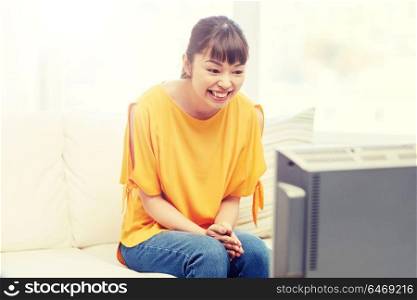 television, entertainment, leisure and people concept - happy asian young woman watching tv at home. happy asian young woman watching tv at home