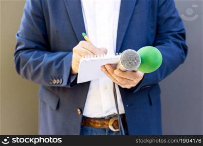 Television journalist or TV reporter at news conference or media event, holding microphone, writing notes