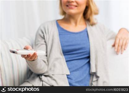 television, leisure and people concept - close up of smiling woman sitting on couch with tv remote control at home