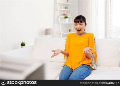 television, leisure and people concept - happy smiling asian woman watching tv at home and having fun. happy asian woman with watching tv at home