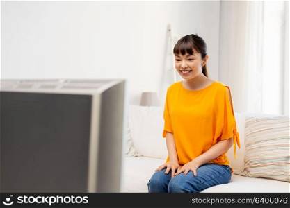 television, leisure and people concept - happy smiling asian woman watching tv at home. happy asian woman with watching tv at home