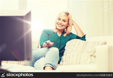 television, leisure and people concept - smiling woman sitting on couch with remote control and watching tv at home. smiling woman with remote watching tv at home