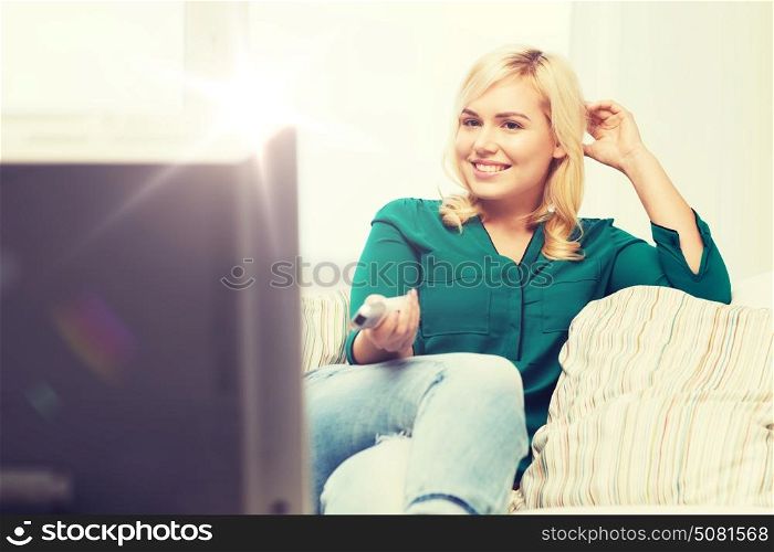 television, leisure and people concept - smiling woman sitting on couch with remote control and watching tv at home. smiling woman with remote watching tv at home