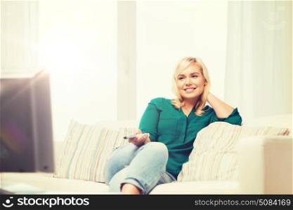 television, leisure and people concept - smiling woman sitting on couch with remote control and watching tv at home. smiling woman with remote watching tv at home. smiling woman with remote watching tv at home