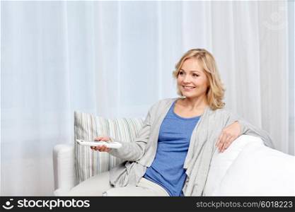 television, leisure and people concept - smiling woman sitting on couch with tv remote control at home