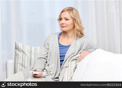 television, leisure and people concept - smiling woman sitting on couch with tv remote control at home