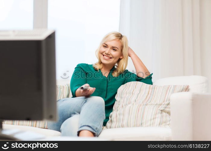 television, leisure and people concept - smiling woman sitting on couch with remote control and watching tv at home