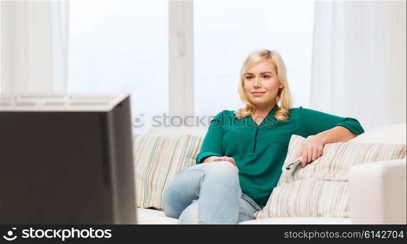 television, leisure and people concept - smiling woman sitting on couch with remote control and watching tv at home