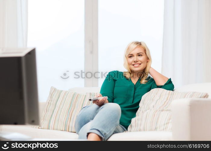 television, leisure and people concept - smiling woman sitting on couch with remote control and watching tv at home