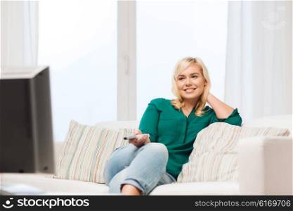 television, leisure and people concept - smiling woman sitting on couch with remote control and watching tv at home