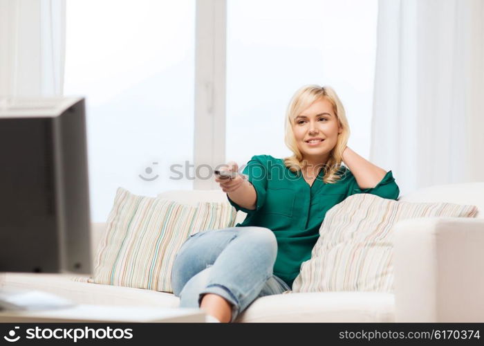 television, leisure and people concept - smiling woman sitting on couch with remote control and watching tv at home