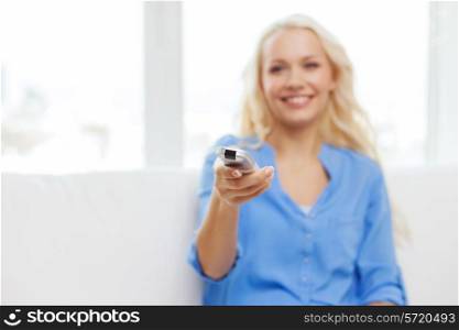 television, relax, home and happiness concept - smiling teenage girl sitting on couch with tv remote control at home