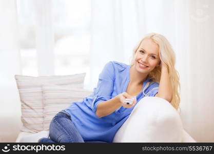 television, relax, home and happiness concept - smiling young girl sitting on couch with tv remote control at home