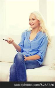 television, relax, home and happiness concept - smiling young girl sitting on couch with tv remote control at home