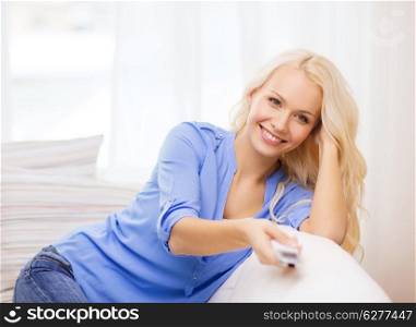 television, relax, home and happiness concept - smiling young girl sitting on couch with tv remote control at home