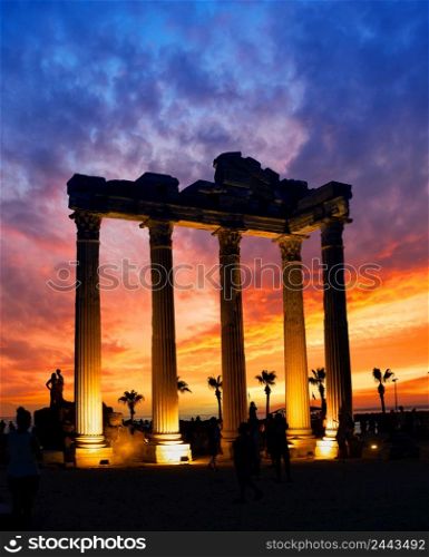 Temple of the Apollo in Side against dramatic sunset sky. Lighted columns. Silhouettes of people. Architectural heritage. A popular tourist destination. One of the main attractions of Turkey. Temple of the Apollo in Side against dramatic sunset sky