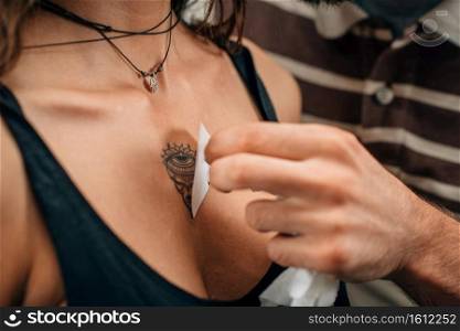 Temporary tattoo. Professional make-up artist applying temporary tattoo sticker to model’s chest