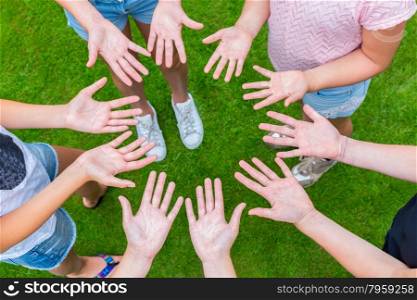 Ten arms of children in circle with palms of hands up above green grass