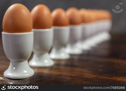 Ten boiled eggs in white egg cups in a line on a wooden table